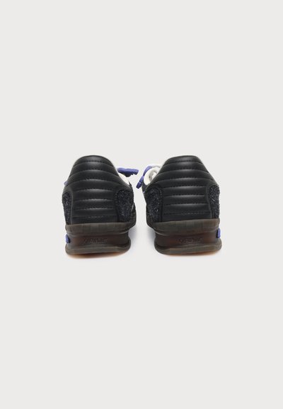 Paire de baskets noires avec panneaux matelassés au talon et détails texturés sur les côtés, vues de dos sur fond blanc.