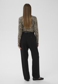 Langärmliges Oberteil mit Leopardenmuster, kombiniert mit schwarzen hoch taillierten Hosen. Das Outfit zeichnet sich durch eine glatte Textur und eine figurbetonte Silhouette aus.