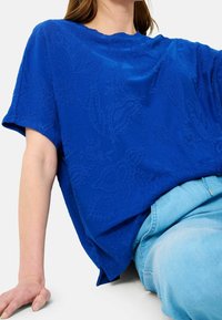 Camiseta de algodón azul con patrones florales en relieve, mangas cortas y un corte holgado. Combinada con unos vaqueros de mezclilla azul claro.