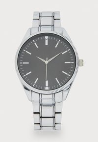 Montre en acier inoxydable argenté avec un cadran rond noir, des index argentés et une lunette texturée. Elle est dotée d'un bracelet en maillons métalliques.