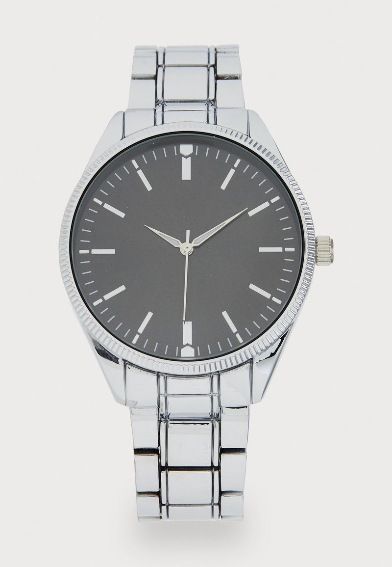 Montre en acier inoxydable argenté avec un cadran rond noir, des index argentés et une lunette texturée. Elle est dotée d'un bracelet en maillons métalliques.