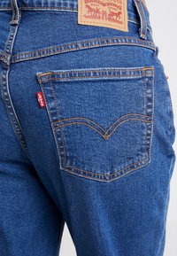 Mörkblå denimjeans med kopparstickningar, en Levi's-märkning vid midjan och en distinkt bakfickdesign med ett V-format mönster.