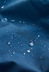 Marineblauwe waterdichte stof met waterdruppels op het oppervlak, met een gladde textuur en glans door lichtreflectie.