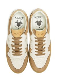 Baskets avec un schéma de couleurs beige et marron clair, fabriquées en daim et cuir, avec des détails perforés et des lacets marron, et un logo sur la languette.