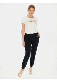 Biała koszulka z okrągłym dekoltem z złotym napisem "L'AMOUR", zestawiona z czarnymi zwężanymi spodniami i beżowymi sneakersami z różowymi akcentami. Gładkie wykończenie tkaniny.