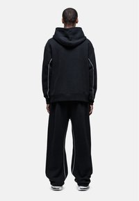 Zwarte oversized hoodie met een trekkoord en contrasterende witte piping, gecombineerd met bijpassende losse broek in een zachte stof.