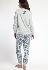 Mujer vistiendo una camiseta de manga larga gris con "Aloha Stitch" y el personaje Stitch en la parte posterior, combinada con pantalones a juego con estampados de Stitch azules.