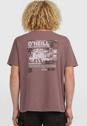 Man with curly blond hair wearing mauve O'Neill t-shirt with vintage-style Santa Cruz surf shop graphic on the back.