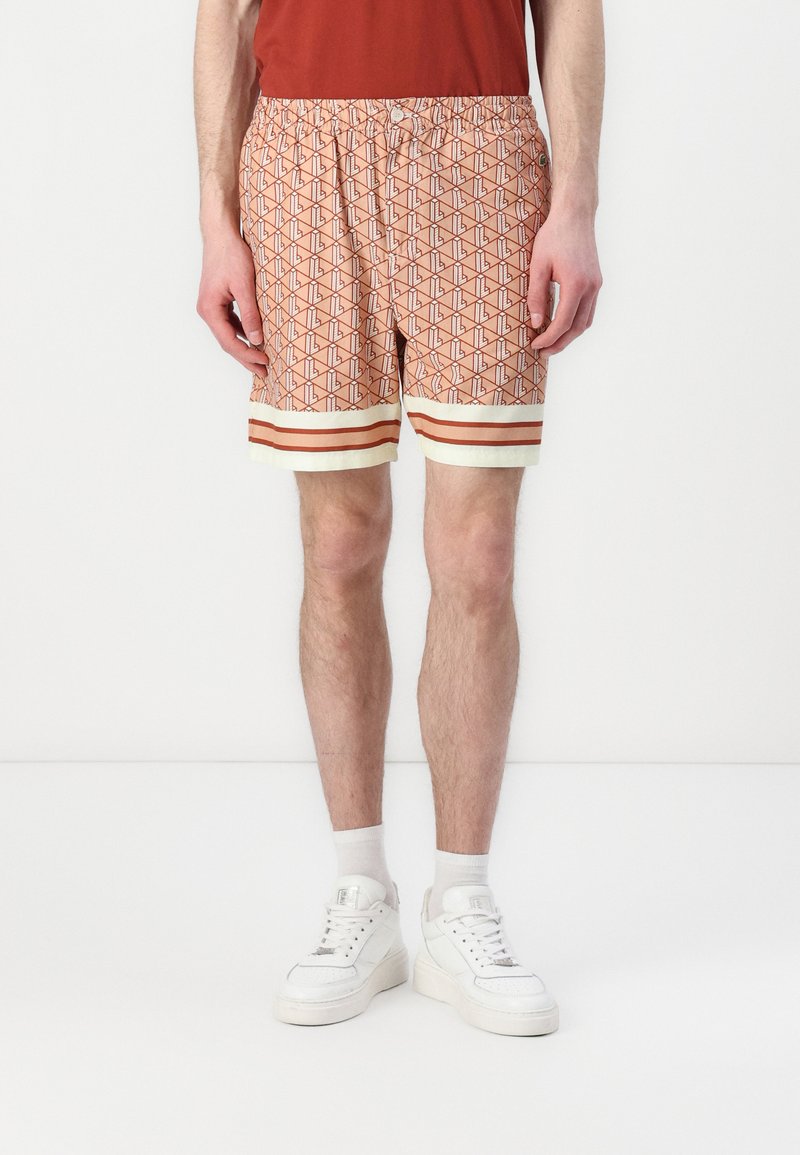 Mønstret badetights i orange med geometrisk design, med elastisk liv, hvit og rød stripet kant, og myk stoff.