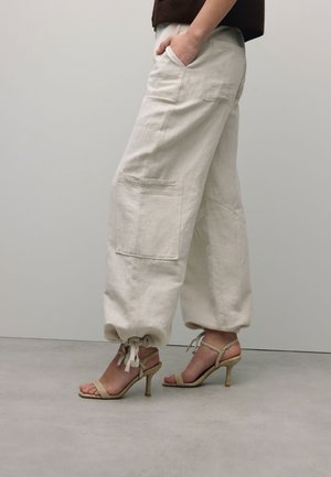 Lichtgekleurde, losse linnen broeken met twee zijzakken en aantrekkoorden bij de enkels. Gecombineerd met sandaaltjes met hakken.