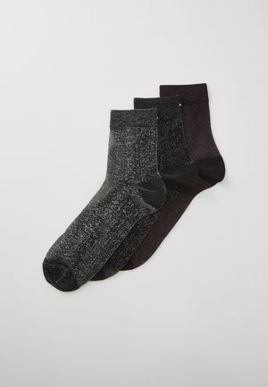 Tre par glittriga ankelsockor i svart, mörkgrå och djup lila, prydligt staplade på en vit bakgrund.