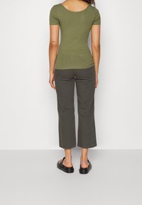 Olivově zelený žebrovaný top s krátkým rukávem, sladěný s tmavě olivovými krátkými kalhotami a černými platformovými sandály. Hladká textura a přiléhavý střih.