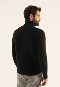 Maglione nero lavorato a maglia con collo alto, tessuto strutturato e polsini a coste. Mostrato dal retro con un design a vestibilità standard.