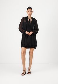 Μαύρο, ημιδιαφανές φόρεμα με φουσκωτό τελείωμα, μακριά μανίκια και λεπτομέρεια με κορδόνι στον λαιμό. Διαθέτει απαλό ύφασμα και επαγγελματική σχεδίαση.