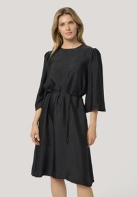 Robe noire, longueur genou, en tissu texturé. Dotée d'un col rond, de manches trois quarts et d'une ceinture à la taille pour un ajustement personnalisé.