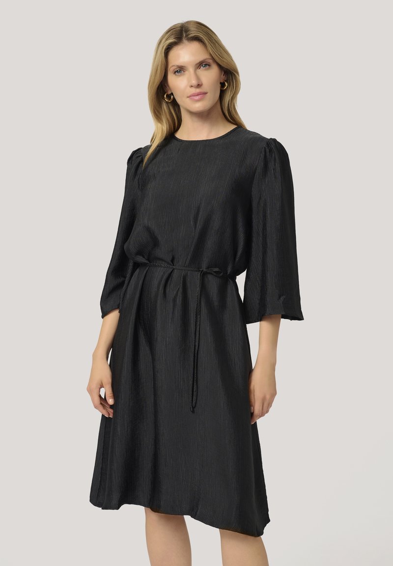 Robe noire, longueur genou, en tissu texturé. Dotée d'un col rond, de manches trois quarts et d'une ceinture à la taille pour un ajustement personnalisé.