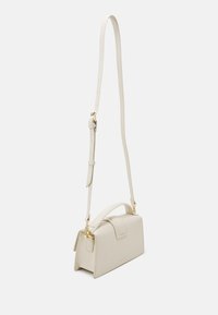 Beige lædertaske med en struktureret form, top-håndtag og justerbar skulderrem. Har guldfarvet hardware og et minimalistisk design.