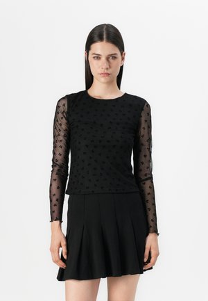 Zwarte top met doorschijnende lange mouwen, voorzien van een textuur met bloemmotief. Het lijfje heeft een effen afwerking, aangevuld met een zwarte flared rok.