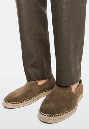 Chaussures espadrilles marron en daim slip-on portées avec un pantalon marron assorti, montrant un gros plan des pieds et des jambes inférieures.