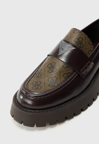 Barna bőrcipő barna és fekete mintás felsőrésszel, fekete logó táblával és masszív, bordázott talppal.