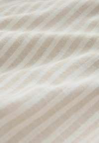 Beige stof met lichte verticale strepen, met een textuur en natuurlijke vezels, waardoor een zacht, subtiel patroon ontstaat.