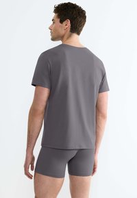 T-shirt gris in cotone con maniche corte e colletto a giro, abbinato a boxer grigi coordinati. Texture liscia e design semplice.