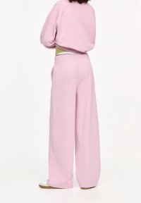 Světle růžové teplákové kalhoty s širokým střihem, elastickým pasem a bočními kapsami. Materiál vypadá měkce a pohodlně.