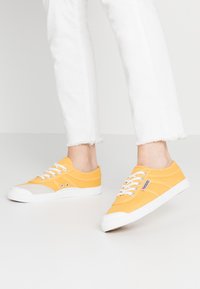 Sneakers in tela gialla con suole e dettagli in gomma bianca. Design classico con lacci, presenta punta e occhielli rinforzati.