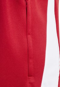 Rote Sportshorts mit einem Reißverschlussfach, strukturiertem Stoff und weißen Seitenpaneelen. Das Material ist glatt und atmungsaktiv.