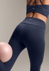 Leggings de culoare bleumarin, fabricate dintr-un material elastic, cu un talie înaltă și branding subtil OYSHO, combinate cu o minge de exerciții de culoare roz deschis.