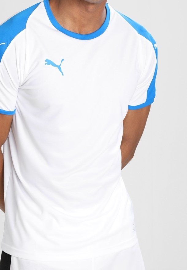 Man som bär en vit sporttröja med blå axlar och kanter, med en blå Puma-logotyp på bröstet.