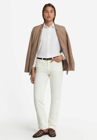Ljusbeige jacka över en vit skjorta med knappar, ihop med vita jeans och bruna sandaler med remmar. Minimalistisk design och rena linjer.