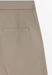 Dos d’un pantalon habillé beige montrant une poche passepoilée simple et une ceinture cousue sur un tissu lisse.
