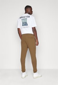 Witte T-shirt met grafische print, met de tekst "BOSSY2K." Bruine joggers met zijzakken en geribde manchetten. Witte sneakers.