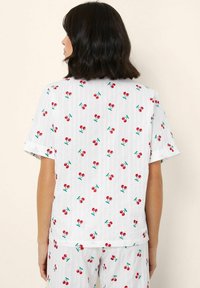T-shirt met korte mouwen van witte stof met een rode kersenprint en groene bladeren, met een relaxte pasvorm en omgeslagen mouwen.