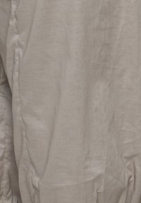 Gros plan sur un tissu beige avec des coutures visibles et de légers plis, montrant la texture et les détails des coutures.