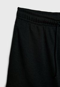 Sorte joggerbukser set ovenfra, med elastisk talje og snøre, glat tekstur og afslappet pasform.