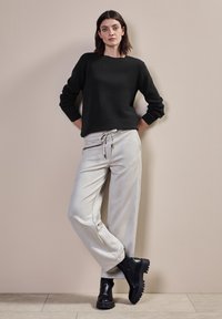 Maglietta nera a maniche lunghe con texture diagonale, abbinata a pantaloni da jogging grigio chiaro con cordino. Stivaletti neri chunky alla caviglia completano il look.