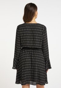 Rochie neagră cu un model geometric în forme de diamant, de culoare aurie și crem, cu mâneci lungi și evazate și o talie elastică pentru un fit relaxat.