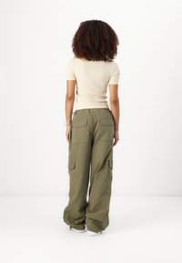Lys beige tettsittende topp med korte ermer og løse olivengrønne cargobukser med flere lommer og avsmalnende hems, mot en hvit bakgrunn.