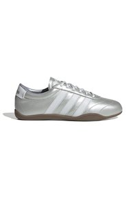 Scarpa sportiva argento con tre strisce bianche, tomaia metallica liscia, punta arrotondata e suola in gomma marrone con motivo a spina di pesce.