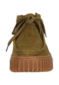 Chaussure en daim vert olive avec un bout arrondi, un col rembourré et des lacets assortis. Semelle en gomme épaisse et nervurée ajoutant texture et hauteur.