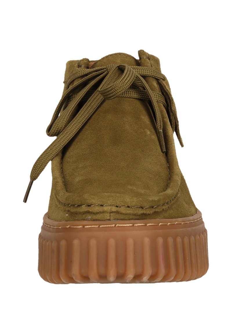 Zapato de ante verde oliva con punta redondeada, cuello acolchado y cordones a juego. La suela de goma gruesa y estriada aporta textura y altura.