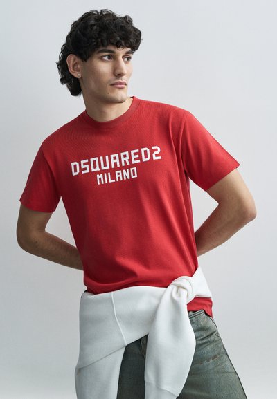 Κόκκινο βαμβακερό t-shirt με την επιγραφή "DSQUARED2 MILANO" σε λευκά γραμματάκια. Το μοντέλο φοράει ένα λευκό φούτερ δεμένο στη μέση.