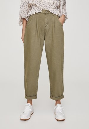 Personne portant un pantalon décontracté olive retroussé, des baskets blanches et un chemisier léger à motif floral avec des détails à volants.
