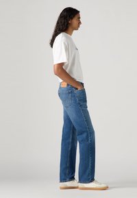 Lichtblauwe denim jeans met een rechte pasvorm, gecombineerd met een witte T-shirt en witte sneakers. Heeft een leren patch op de achterkant van de tailleband.
