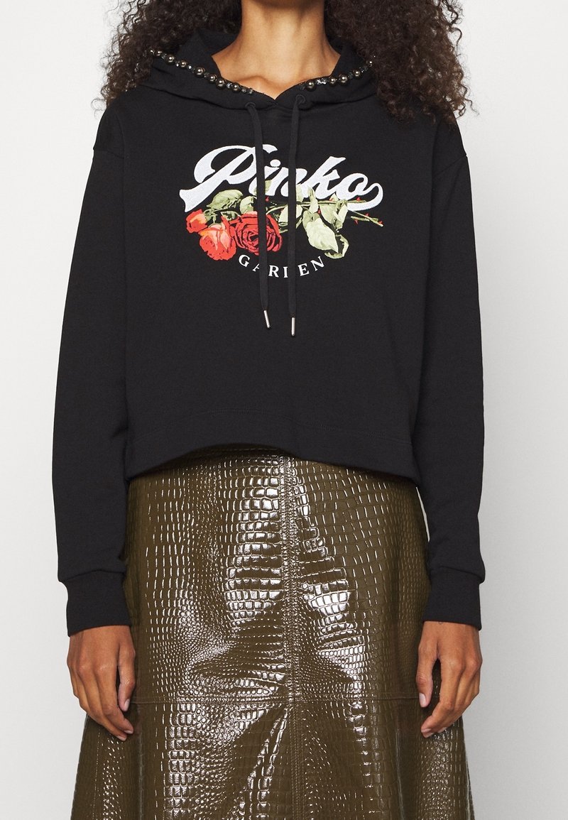 Sweat à capuche noir avec imprimé floral "Pinko Garden" et capuche cloutée en métal, associé à une jupe brillante vert olive texture croco.