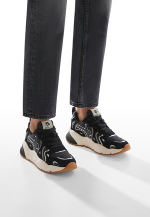 Scarpe da ginnastica nere realizzate in materiali scamosciati e in rete, con accenti riflettenti, una suola imbottita color crema e una suola in gomma naturale.