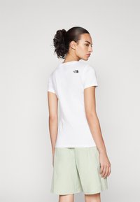 Hvid kortærmet t-shirt med rund hals og et lille sort logo på den øverste del af ryggen. Matchet med lysegrønne shorts. Glat tekstur.