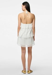 Robe blanche à plusieurs niveaux avec un col halter et un dos nu. Tissu léger et transparent avec une silhouette fluide et de subtils détails en volant.